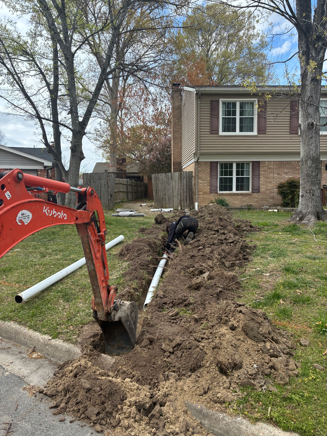 Mini excavator and crew installing drainage pipe in a residential yard
