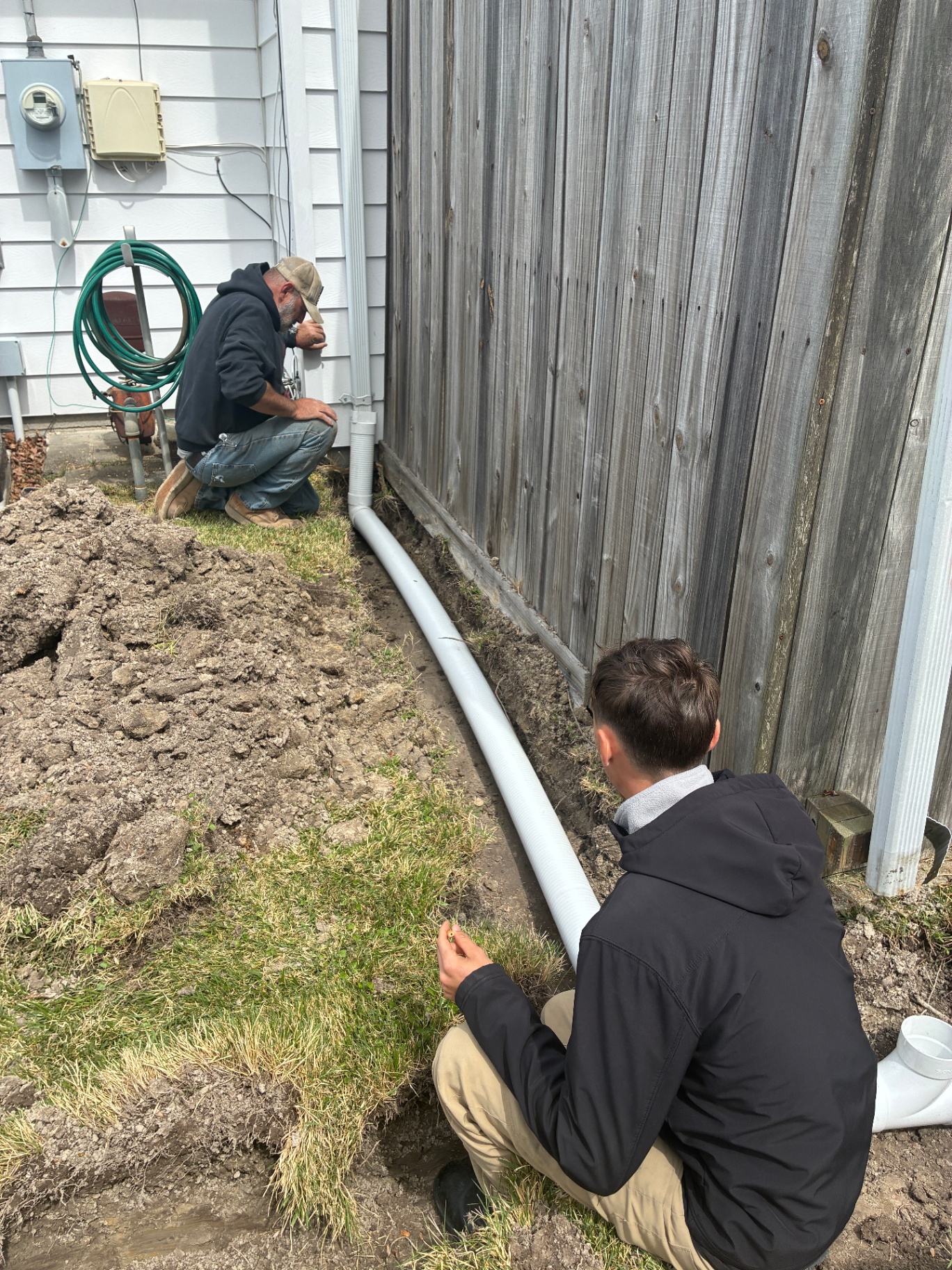 Dave and a crew member connecting drainage pipe beside a home