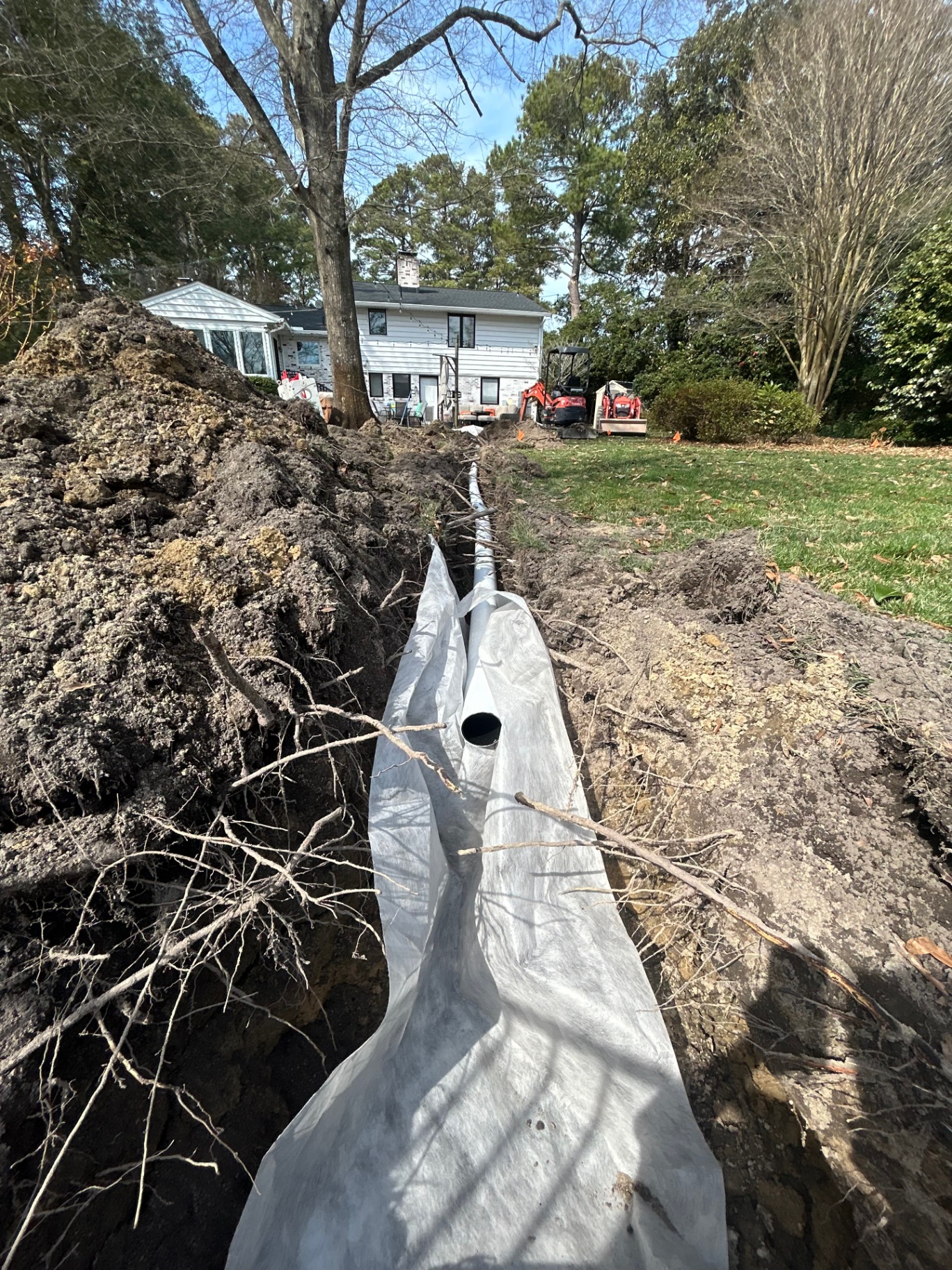 French drain pipe wrapped in fabric placed in a deep trench across a yard